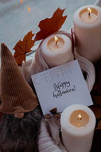 万圣节快乐文本贺卡概念在舒适的家中庆祝秋季假期在窗台上 Hygge 美学氛围秋叶香料和蜡烛在针织白色毛衣上温暖的黄色灯光。