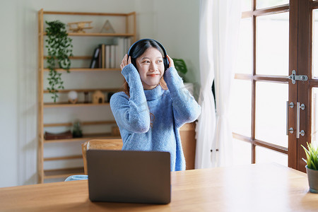 一名亚洲少女使用电脑、戴着耳机通过家里木桌上的视频会议在线学习的肖像