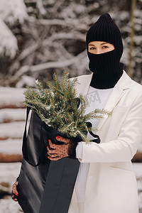 除夕夜，一个穿着白色西装和巴拉克拉法帽的女孩带着一包圣诞树在冬季森林里。新年的概念