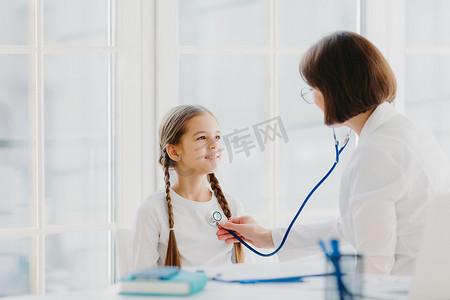 可爱的小女孩听专业经验丰富的医生的咨询，用听诊器听她的肺部，来进行体检预约。