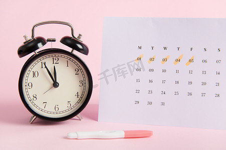静物画：闹钟、日历和pinp背景上的妊娠测试。