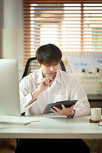 穿着白衬衫的男经理集中精力坐在办公桌前检查财务报告