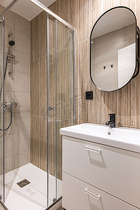 浴室玻璃摄影照片_小浴室的特写镜头，配有时尚的白色玻璃淋浴柜和带黑色水龙头和时尚米色瓷砖的陶瓷水槽。
