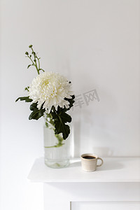 玻璃花瓶里插着一朵大菊花，两杯有凹槽的咖啡，桌子上还有陶瓷小鸟雕像。