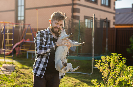 年轻人在后院的房子附近抱着杰克罗素梗犬 — 宠物主人和动物