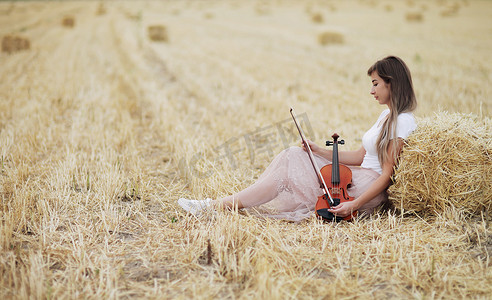 拿小提琴摄影照片_田野里，头发飘逸的浪漫年轻女子手里拿着小提琴
