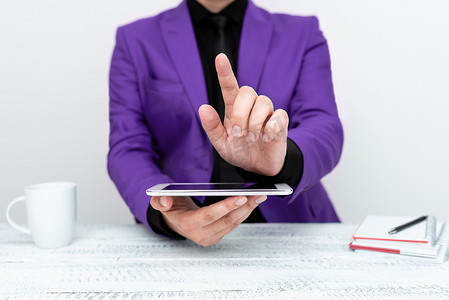 紫色商务摄影照片_身穿紫色夹克的商人坐在桌旁，拿着手机，用一根手指指着重要消息。