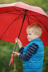 秋天雨天摄影照片_雨天户外有红色雨伞和蓝色夹克的可爱小男孩。