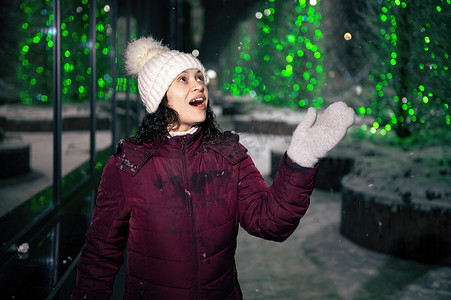 美丽的女人捕捉雪花，喜欢沿着城市街道漫步，在下雪的冬夜被花环照亮