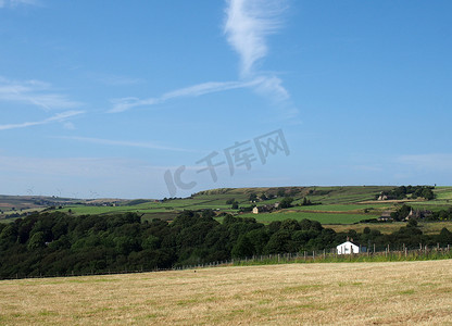 蓝色天空摄影照片_西约克郡卡尔德代尔的卢登登村上方，一片被绿色田野和农舍环绕的夏季干草草地，阳光明媚的蓝色天空