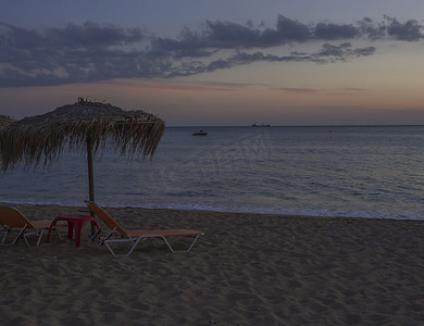 希腊科孚岛的 Agios Georgios Pagon 海滩在蓝色时刻，日落后深蓝色和橙色的云彩，太阳伞空荡荡的日光浴床和船和船，平静而安宁的场景。