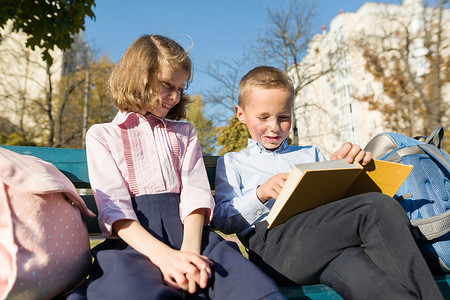 小男孩和女孩小学生读书，坐在长凳上，背着背包的孩子