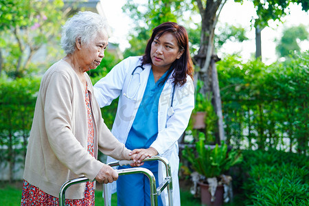 医生帮助亚洲老年妇女残疾患者在公园里用步行器行走，医学概念。