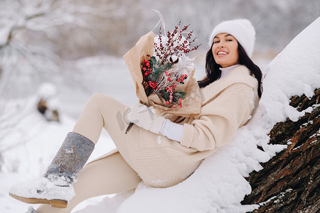 一个穿着米色羊毛衫和冬花的女孩在雪季在大自然中行走。