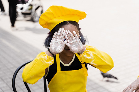 黑人厨师摄影照片_非洲黑人厨师小女孩手上拿着面粉，闭上脸。