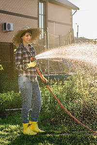 阳光明媚、温暖的夏日，身着工作服的女园丁在菜园里浇水。