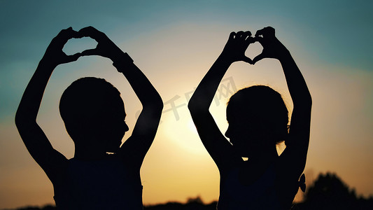 人拥抱剪影摄影照片_夏天日落时，孩子、男孩和女孩的剪影、形象用手指、手在太阳的背景下展示了心。