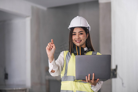 快乐专业建筑工程师女性手持笔记本电脑、戴安全帽在建筑工地背景、工业工程概念的肖像