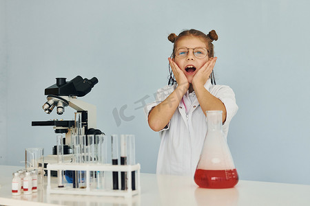 穿着外套的害怕的小女孩在实验室里用设备扮演科学家
