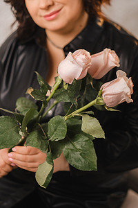 皮衣摄影照片_一位穿着黑色皮衣的时尚成年女性站着，里面放着一束粉红玫瑰