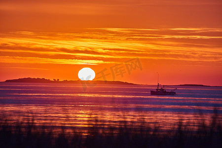 海洋东海岸的日出，金色的光芒，前景是草地海岸，远处是渔船