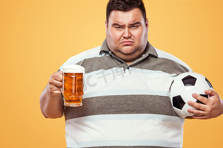足球乐趣 — 慕尼黑啤酒节上悲伤而肥胖的男人，在黄色背景下拿着啤酒和足球。