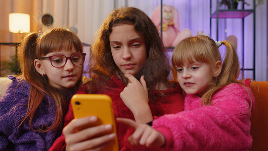 三个兄弟姐妹儿童女孩使用智能手机在社交媒体应用程序上在线发送短信