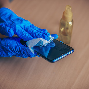 戴蓝色手套的妇女手消毒清洁智能手机