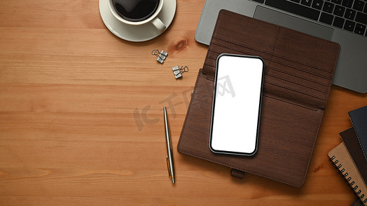 木制办公桌配有智能手机、皮革个人管理器和笔记本电脑。