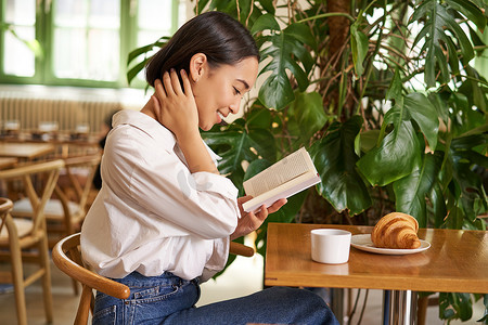 温柔、美丽的亚洲女孩坐在咖啡馆里看书，一边读书一边喝咖啡。