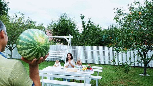 请客摄影照片_夏天，花园里，爸爸背着一个大西瓜，准备请客。