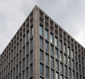 一栋典型的野兽派风格的 20 世纪 60 年代混凝土办公楼的角落细节，带有几何混凝土框架，与灰色多云的天空相映衬