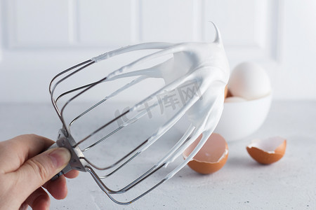 搅拌蛋清 — 用钢丝搅拌器搅打意大利蛋白酥皮，灰色背景上的鸡蛋。
