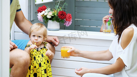 夏天，在花园里，父母和年幼的孩子们玩耍，一个女孩和一个男孩，在咖啡馆里，在儿童游乐屋里，用鲜榨果汁招待孩子们，喝果汁。