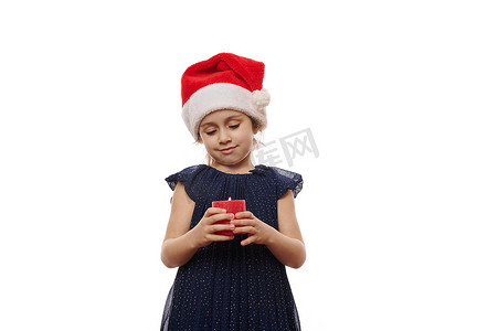 可爱的小女孩穿着圣诞老人的帽子和深蓝色的裙子，在白色背景上摆着点燃的红色蜡烛。