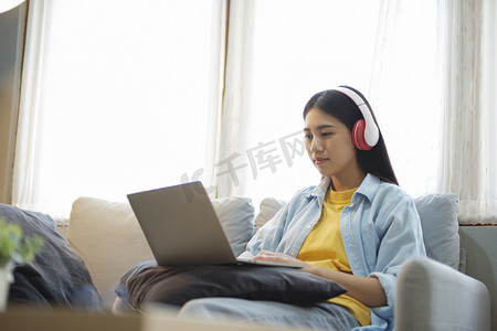 年轻的亚洲女性坐在家里的沙发上学习和听音乐。