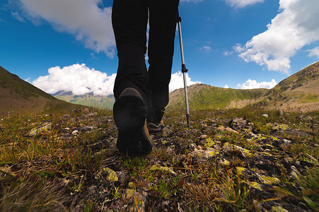 穿着靴子、带登山杖的游客的腿特写，在山上的石头上徒步旅行