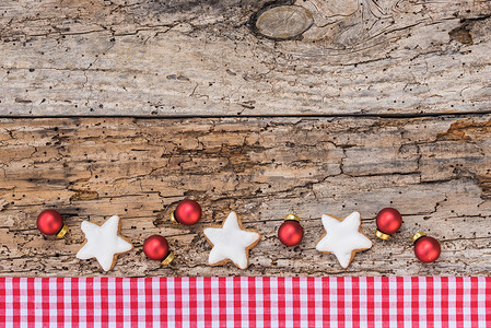 旧木桌上的圣诞星形饼干、球和红色格子织物边框、复制空间