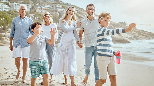 同舟共济共同抗疫摄影照片_快乐的白人小男孩吹、捕捉和爆破肥皂泡，同时与父母和祖父母在海滩享受轻松有趣的暑假的美好时光。
