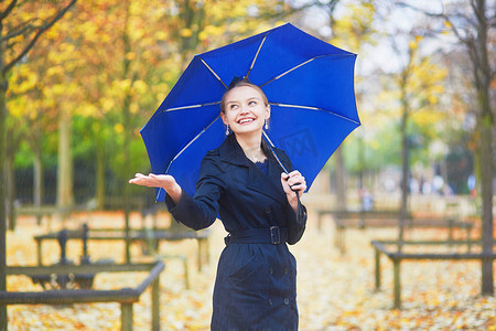 秋季或春季雨天，巴黎卢森堡花园里带蓝色雨伞的年轻女子