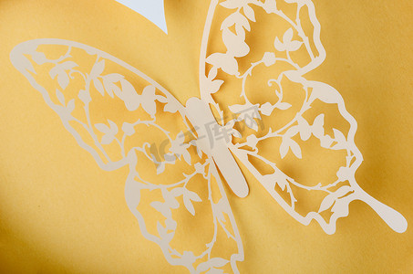 关闭一只纸蝴蝶雕刻在黄色背景上，空间空旷。