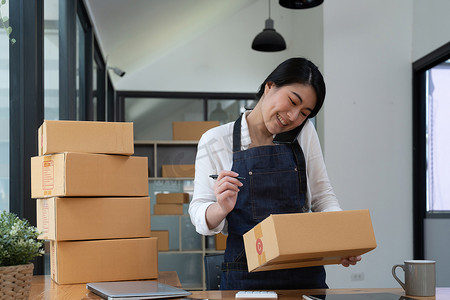 快乐的年轻亚洲女性在家创办小企业自由职业者，家里有包裹箱。