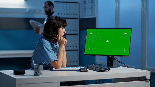 医疗助理站在办公桌前，看着带绿屏显示屏的电脑