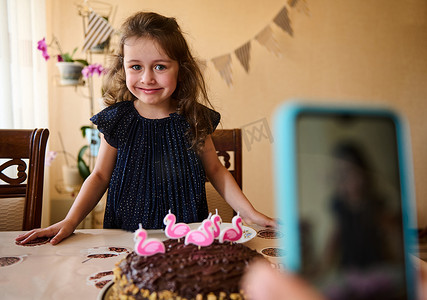 前景模糊的智能手机录制一个身穿海军服的生日女孩吹灭节日蛋糕上蜡烛的视频