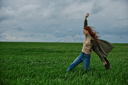 阴天，一个穿外套的女人站在田野里，抵御强风