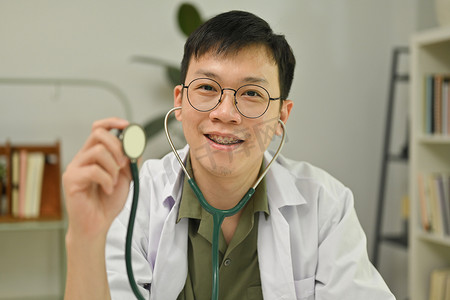 穿着白大褂的亚洲医生拿着听诊器，对着镜头微笑的头像。