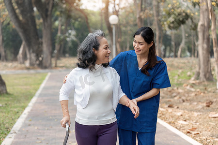 护士用助行器帮助老年妇女 护士牵着手帮助老年妇女在公园设施中行走