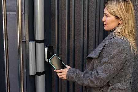 门智能锁摄影照片_妇女使用智能手机将智能锁锁在入口门上。