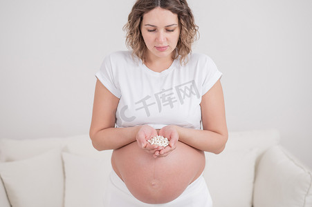 一名孕妇拿着一把白色药丸。