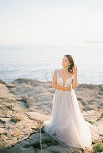 穿着白色蓬松连衣裙的新娘站在岩石海岸上